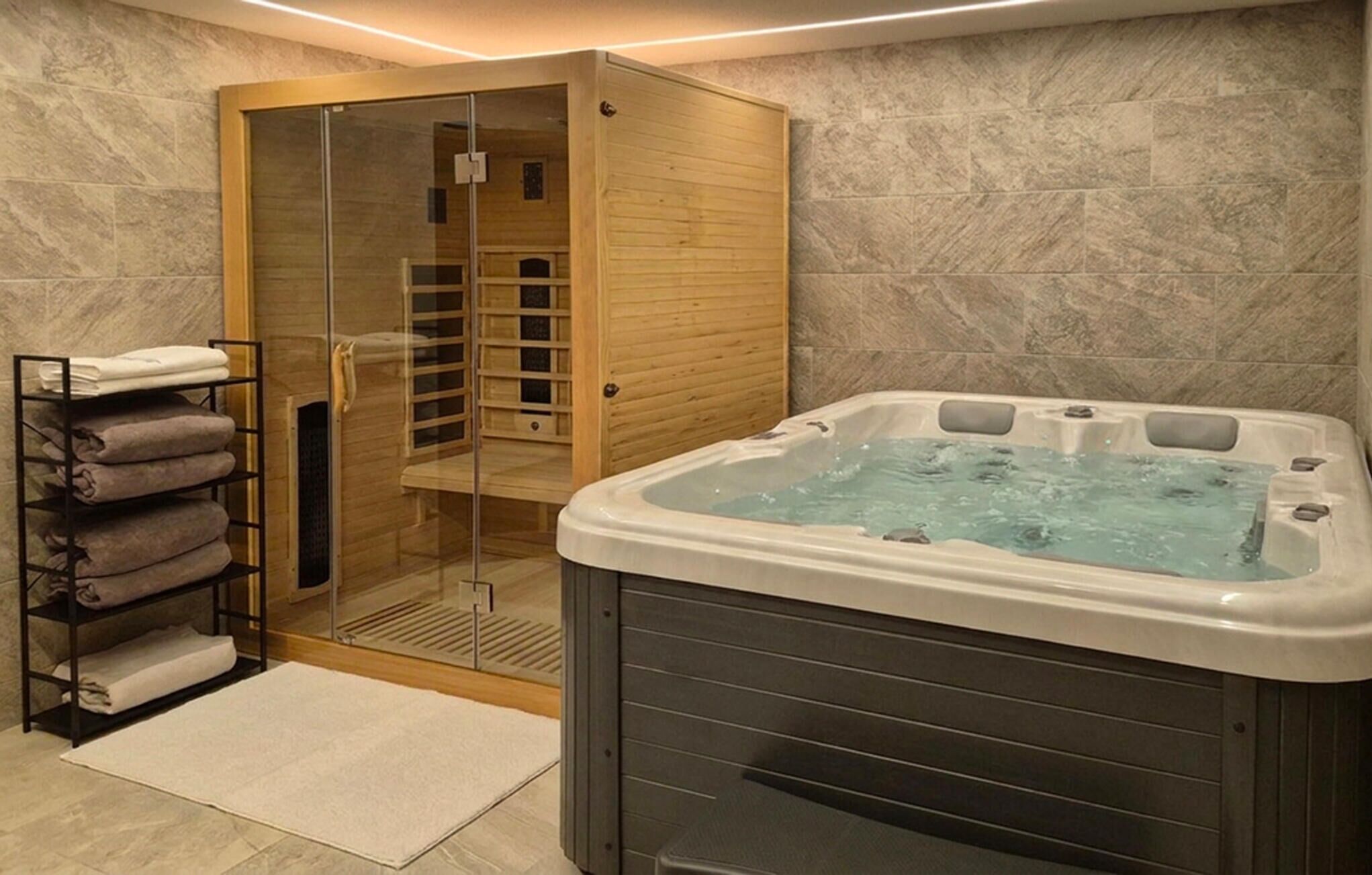 A spa room with a glass-enclosed sauna, a hot tub, and a towel rack with folded towels.