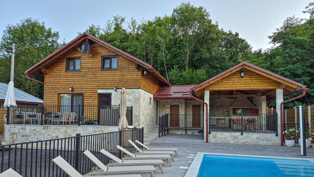 Una cabaña de madera con piscina, paredes de piedra y un porche cubierto.