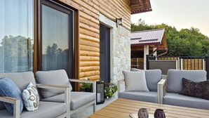 Un espacio al aire libre moderno con sofás y una mesa de centro, que incluye una terraza de madera y una pared de piedra.