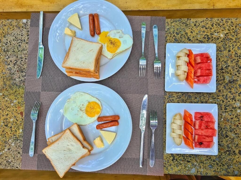 Two plates with toast, eggs, and sausages, and two plates with watermelon and bananas.