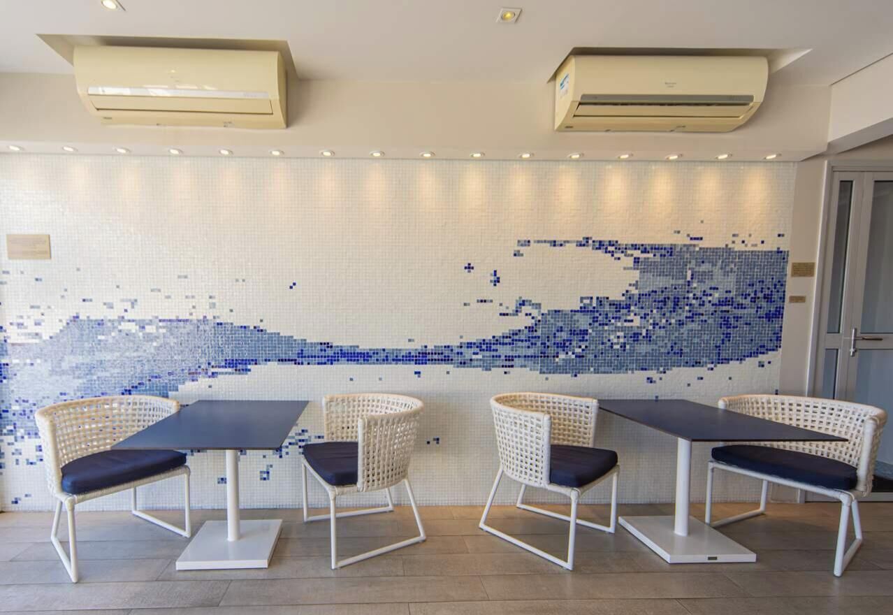 A dining area with a mosaic wall, three wicker chairs, and two air conditioning units.