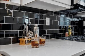 Eine Küche mit schwarzem Fliesenrückwand, einer weißen Arbeitsplatte, einer Kaffeemaschine, einer Flasche und zwei Gläsern.