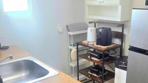 A kitchen with a stainless steel sink, a coffee maker, a refrigerator, and a shelf unit. - #15 Guest house Midtown stadium B (Tampa)