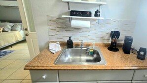 A compact kitchen with a stainless steel sink, a countertop with a soap dispenser, a coffee maker, and a small shelf above the sink. - #15 Guest house Midtown stadium B (Tampa)