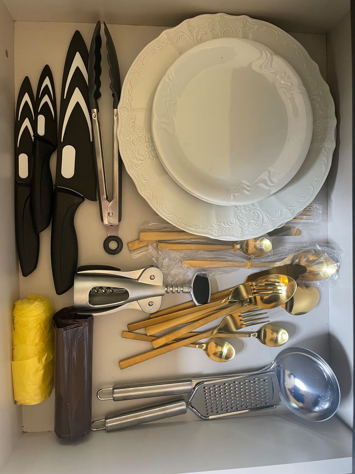 A drawer with various cutlery, including knives, forks, spoons, and a grater.