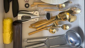 Eine Schublade mit verschiedenen Besteckstücken, darunter Messer, Gabeln, Löffel und eine Reibe.