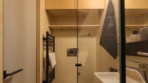 Ein kleines Badezimmer mit Glastrennwand, Toilette, Waschbecken und Handtuchhalter.