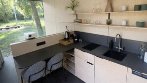 Eine moderne Küche mit einem großen Fenster, zwei Stühlen, einer Spüle und einer Arbeitsfläche mit Wasserkocher und Kaffeemaschine.