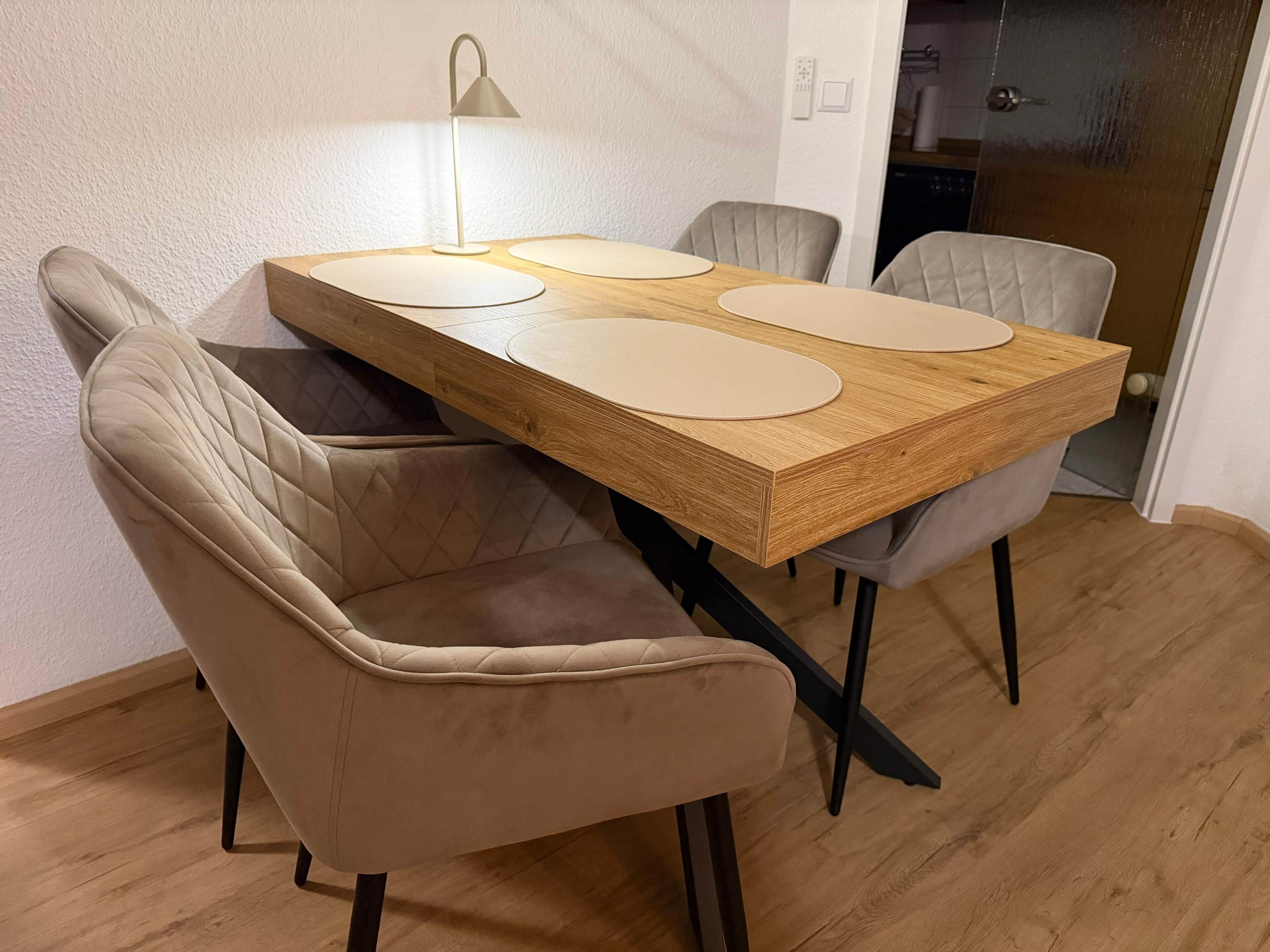 A dining table with four chairs, a lamp, and a wooden floor.