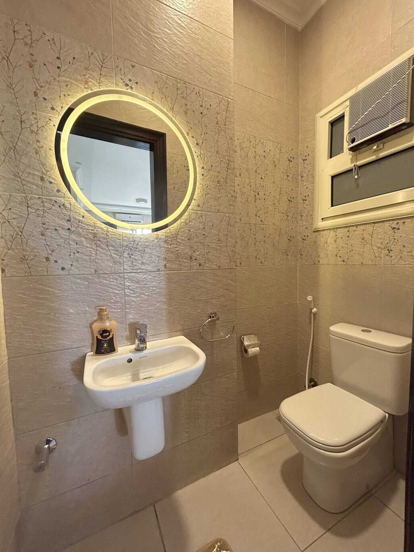 A bathroom with a sink, toilet, and a mirror with a circular light.