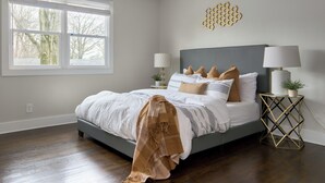 Ein Schlafzimmer mit einem Bett, einem Deckenventilator, einem Fenster, einem Nachttisch mit Lampe und einem dekorativen Wandbild.