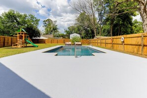 Patio trasero con piscina, valla de madera y estructura de juegos.