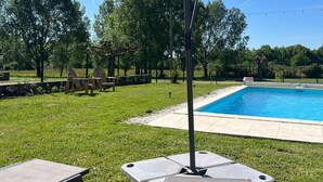 Une piscine avec un espace gazonné, des chaises longues et une pergola dotée d’un auvent.