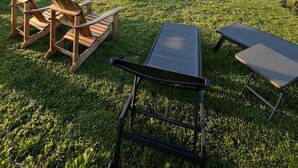Un jardin avec une piscine, des fauteuils Adirondack en bois et une table en métal.