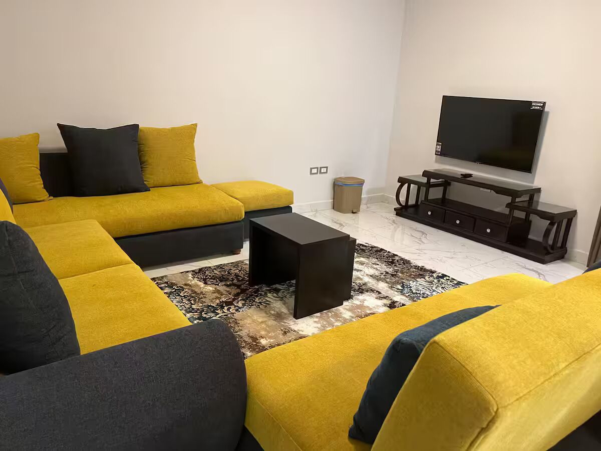 Una sala de estar con un sofá modular, una mesa de centro, un televisor y una mesita auxiliar.