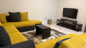 A living room with a sectional sofa, a coffee table, a TV, and a small side table. - Elite House: Cozy Garden Oasis 3BR – Mall of Arabia (Giza Governorate)