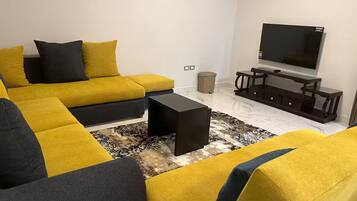 Una sala de estar con un sofá modular, una mesa de centro, un televisor y una mesita auxiliar.