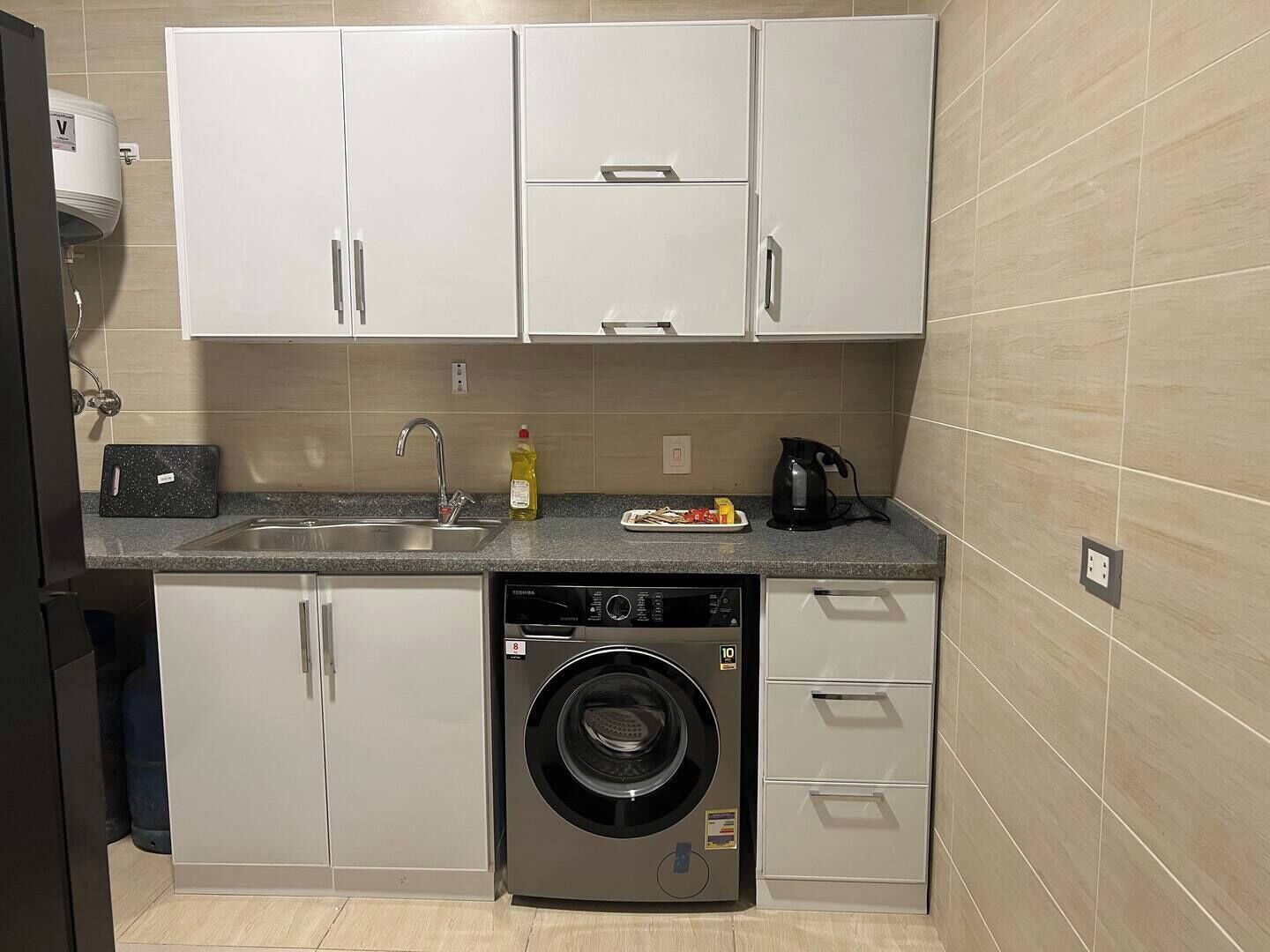 Una cocina compacta con lavadora, un lavamanos y armarios.