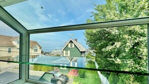 Vista attraverso una finestra su una zona residenziale con case, un'auto e cielo sereno.