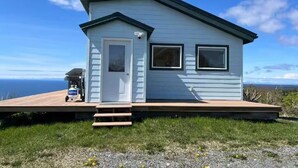 A small, light blue cabin with a deck, a door, and two windows.