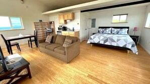 A bedroom with a bed, a sofa, a dining table, and a kitchen area.
