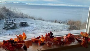 A view through a window of a snowy landscape with a chair and a tire on the deck.