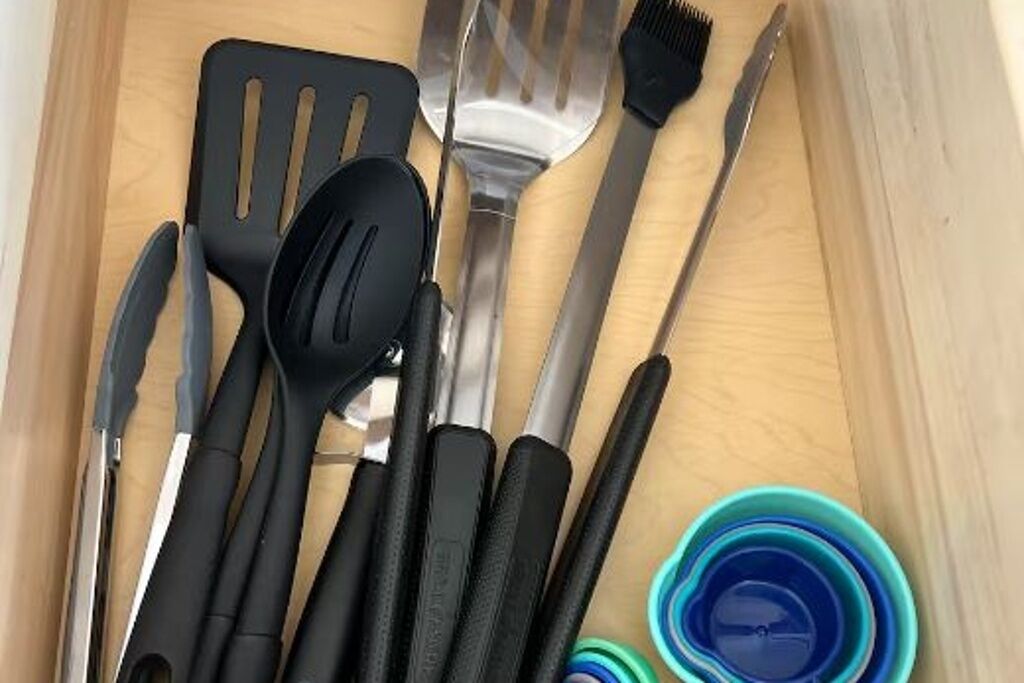 Un tiroir contenant divers ustensiles de cuisine, notamment une spatule, une fourchette, un couteau et une brosse.