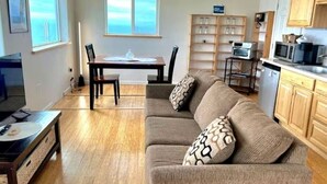 A living room with a sofa, a dining table, and a kitchen area with cabinets and appliances.