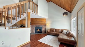 Ein geräumiger Wohnbereich mit Kamin aus Stein, einer Ledersofa und einer Holztreppe, sowie einer hängenden Leuchte.