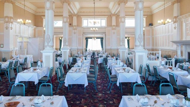 A banquet hall with rows of tables, white drapery, and classical columns. - Hydro Hotel (Llandudno)