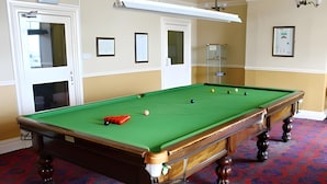 A pool table with balls, a red cue, and a patterned carpet in a room with doors and framed pictures on the walls. - Hydro Hotel (Llandudno)