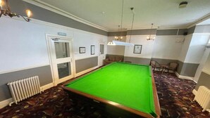 A pool table in a room with patterned carpet, a radiator, and framed pictures on the wall. - Hydro Hotel (Llandudno)
