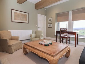 Un salon avec une table basse en bois, des fauteuils beiges, une table à manger en bois et une fenêtre donnant sur un beau paysage.