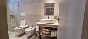 Uma casa de banho moderna com cabine de duche em vidro, um bidé, uma sanita, uma pia com espelho e um porta-toalhas.