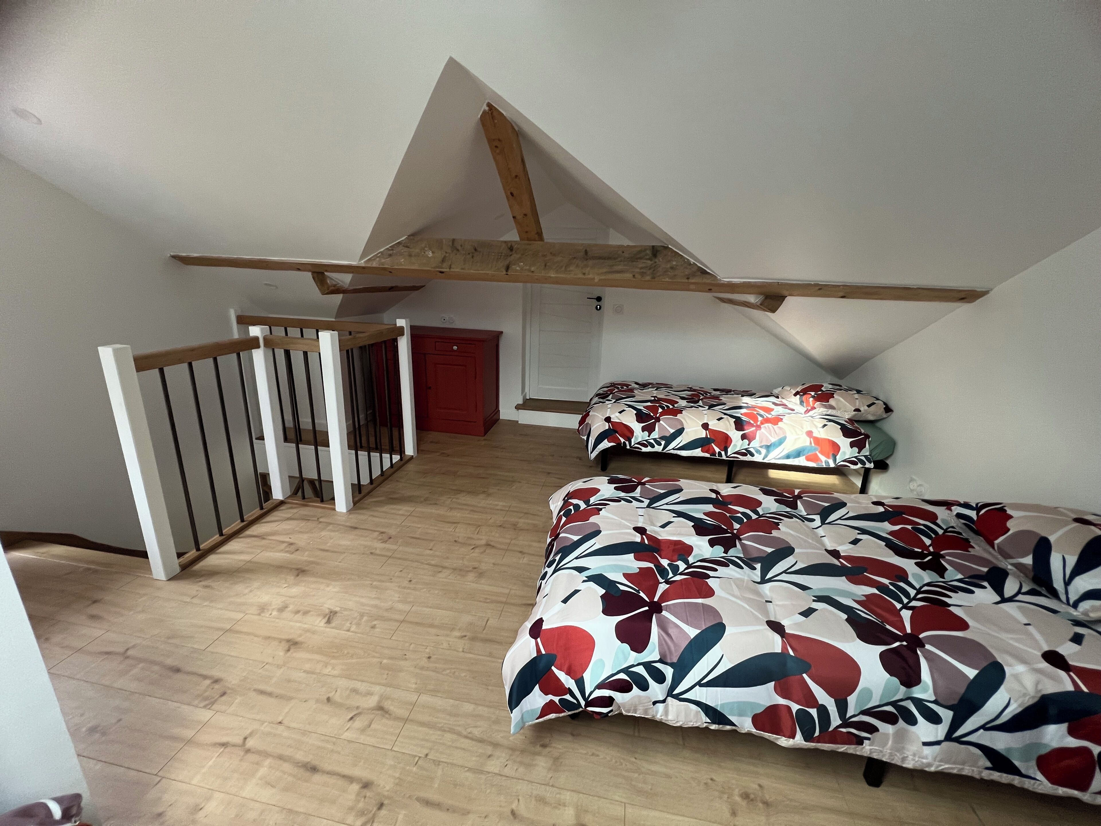 A bedroom with a sloped ceiling, a wooden bed frame, a red cabinet, and a white door.