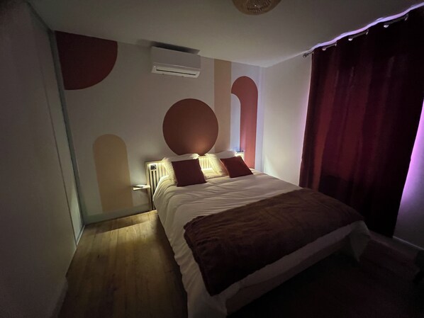 Une chambre à coucher avec un lit, un climatiseur fixé au mur et une grande fenêtre avec des rideaux.
