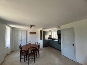 Un comedor con una mesa redonda y sillas, una cocina con ventana, y una puerta que da a otra habitación.
