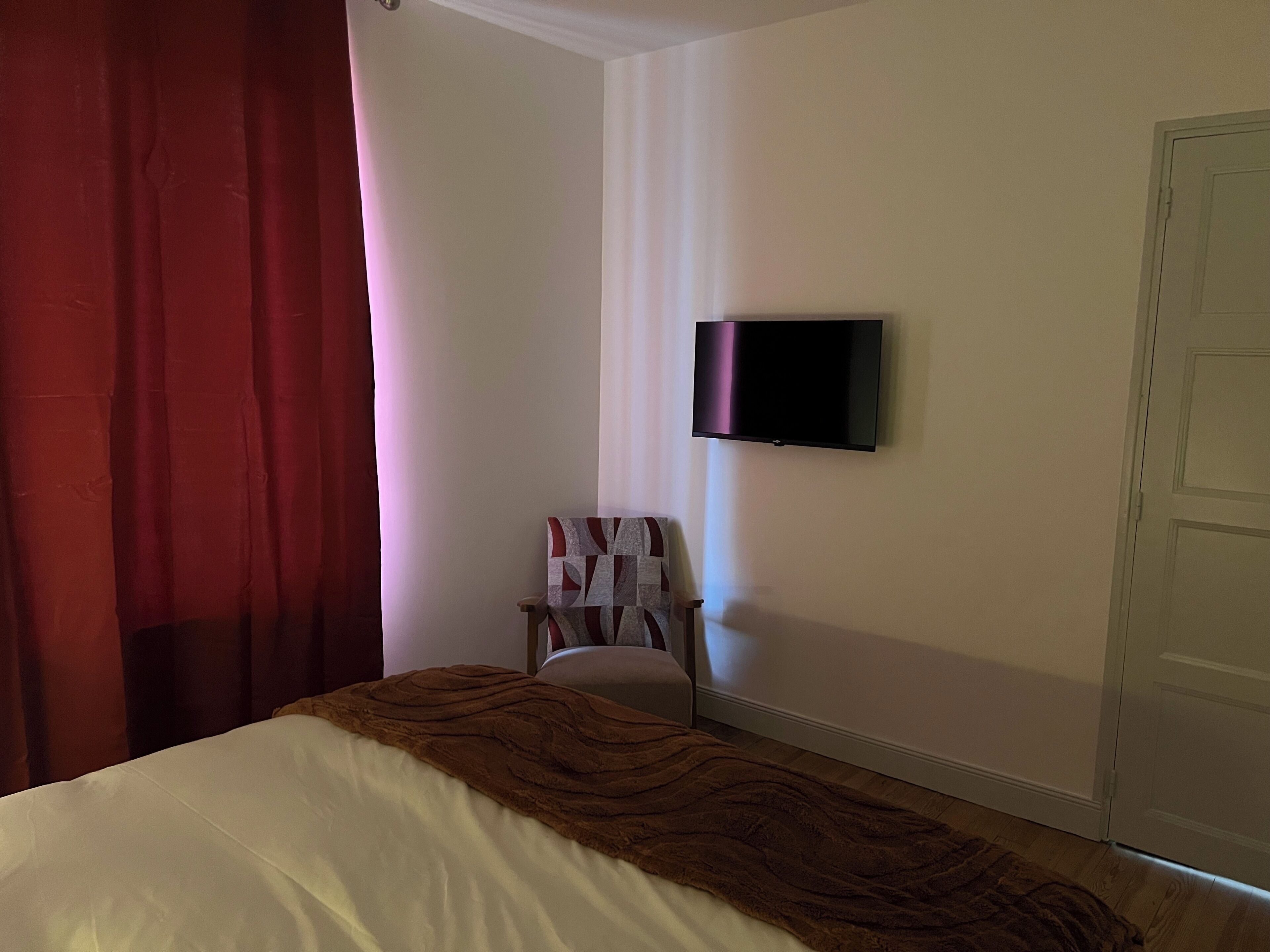 Een slaapkamer met een bed, een aan de muur bevestigde televisie, een stoel en een deur.