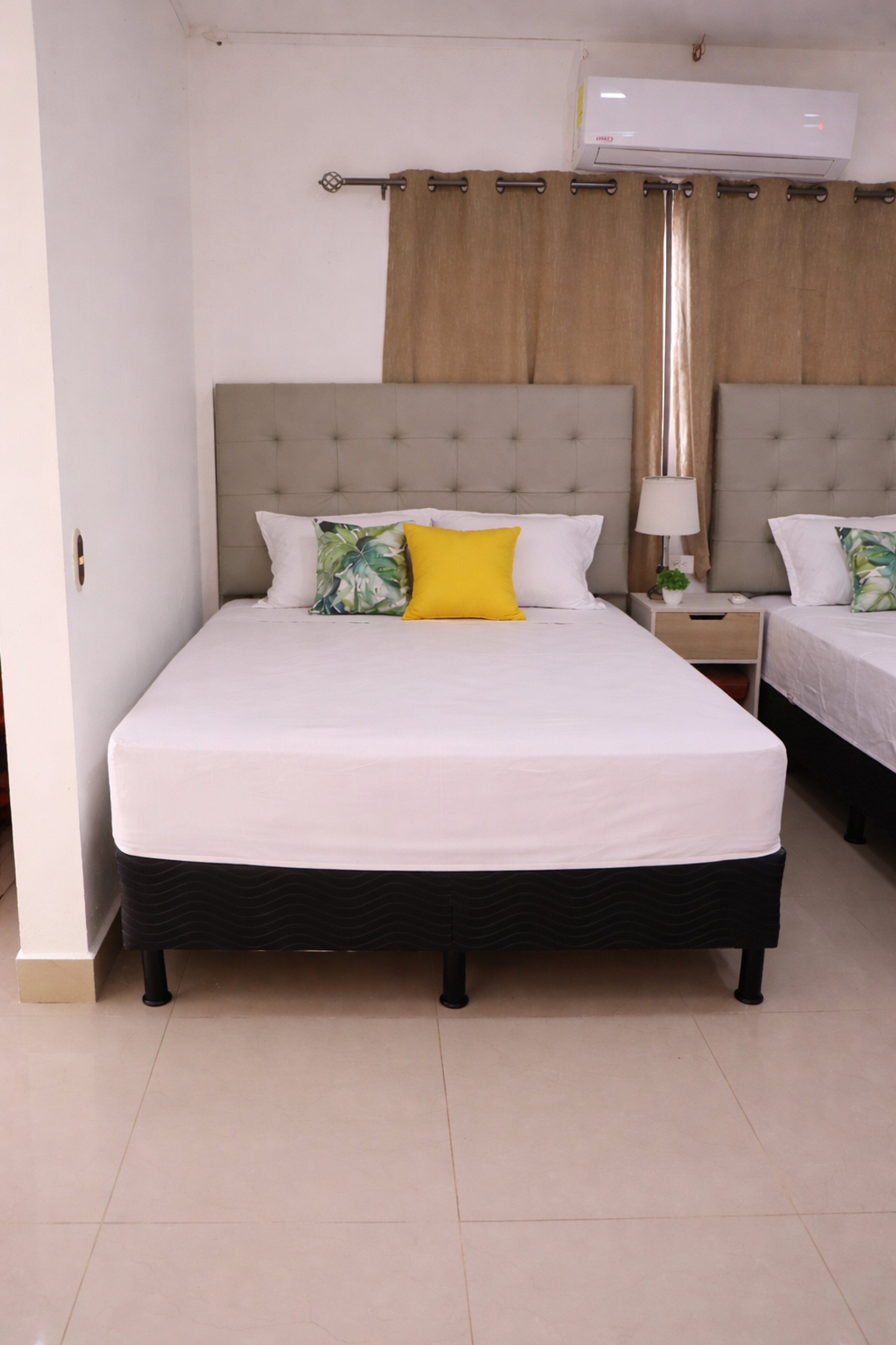 A hotel room with a large bed, a bedside table with a lamp, and an air conditioning unit.