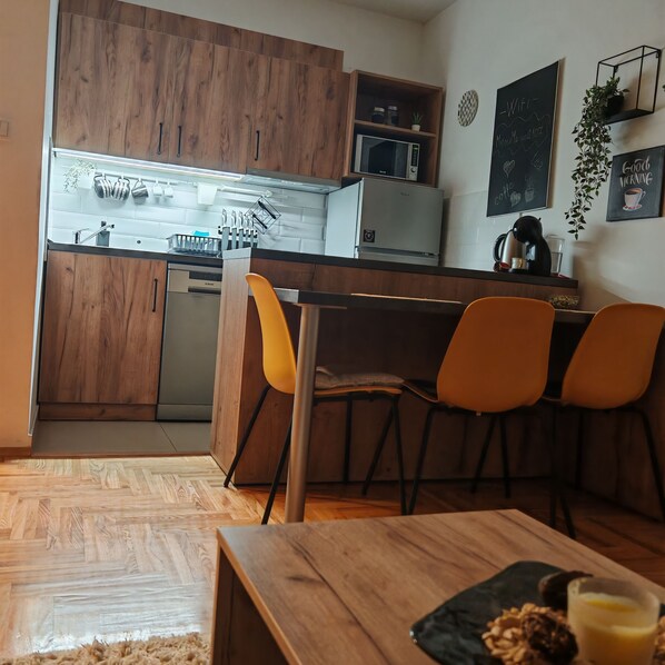 Une cuisine moderne avec des meubles en bois, un four à micro-ondes et un évier. On y trouve deux chaises orange et une table en bois sur laquelle sont posés une assiette de nourriture et un verre de jus de fruits.