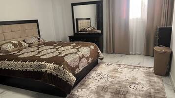 A bedroom with a bed, a dresser, a mirror, a waste basket, and a patterned rug.