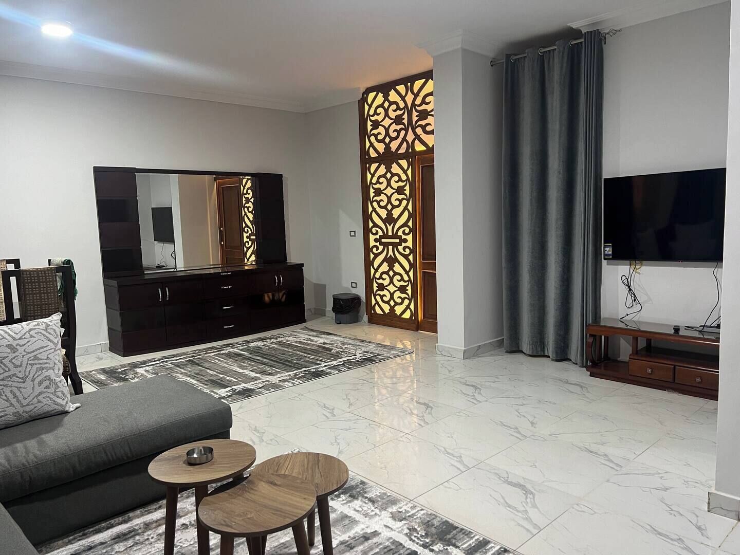 A modern living room with a sofa, a TV, a dark wooden cabinet, a patterned rug, and a decorative wall panel.