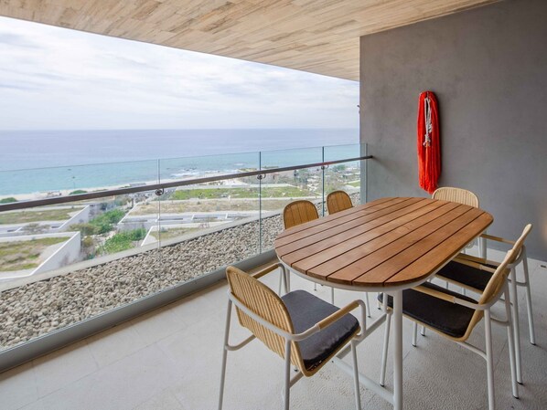 A balcony with a wooden table and wicker chairs, overlooking a coastal view.