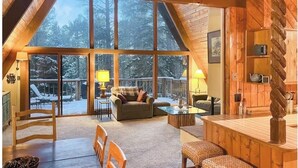 Interior acogedor de una cabaña con un ventanal grande, muebles de madera y una chimenea.
