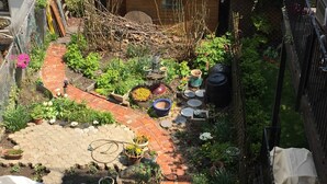 A garden with a brick pathway, potted plants, a small wooden structure, and a metal fence. - Spacious 4-bedroom house in beautiful Hoboken. 20 min to Manhattan and Soccer! (Hoboken)