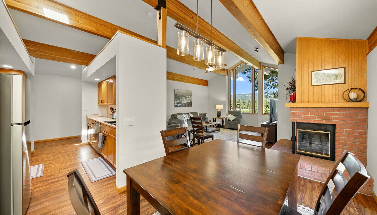 A spacious dining area with a wooden table and chairs, a kitchen with wooden cabinets, and a fireplace with a brick surround.