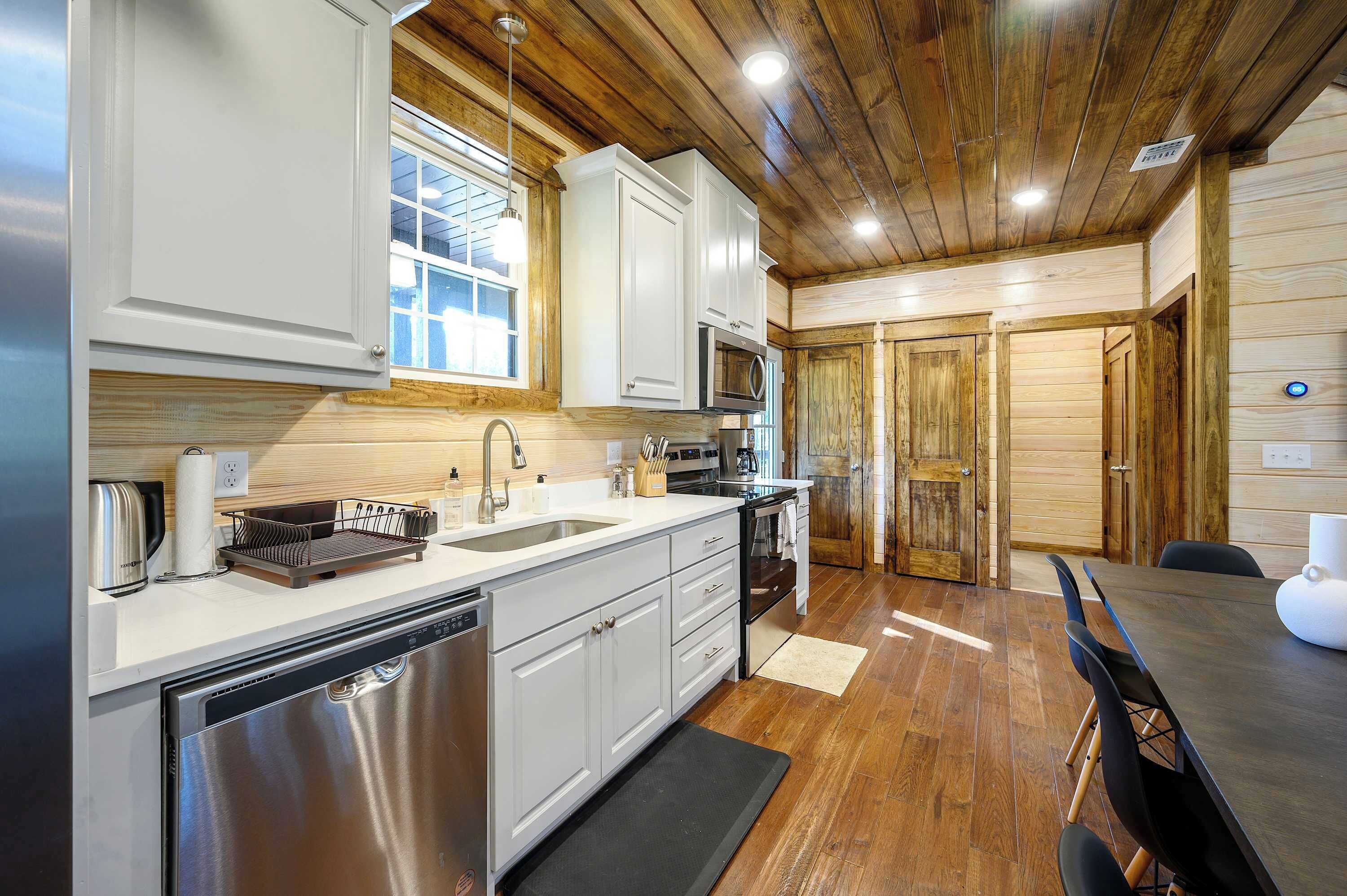 A modern kitchen with white cabinets, stainless steel appliances, and a wooden ceiling.
