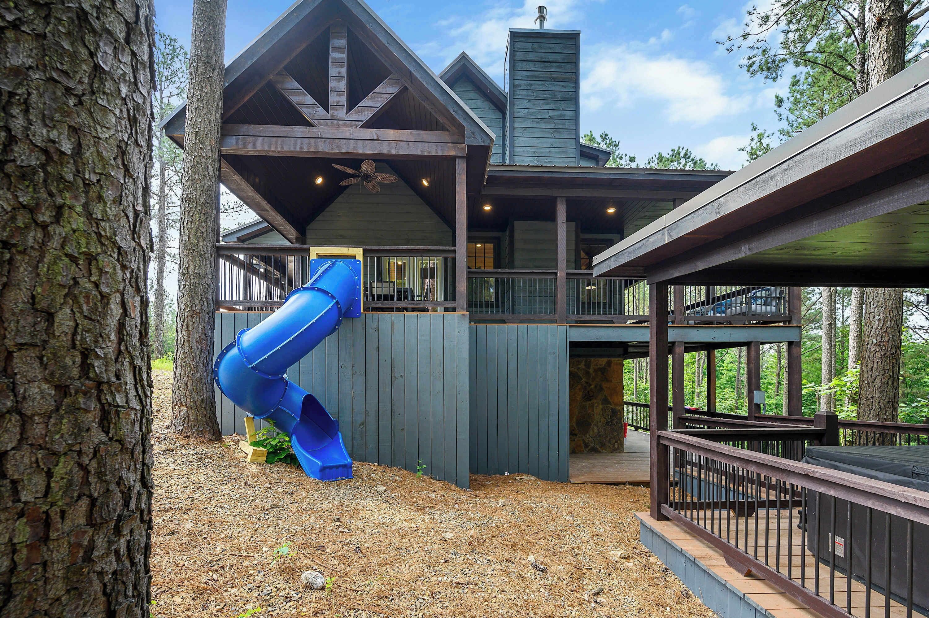 Une cabane avec une façade en bois, un toboggan bleu et une terrasse.