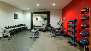 Et fitnessrum med træningsudstyr, et spejl og en rød væg.