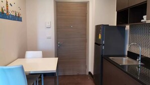 Een kleine keuken met een witte tafel en stoelen, een houten deur en een zwarte koelkast.